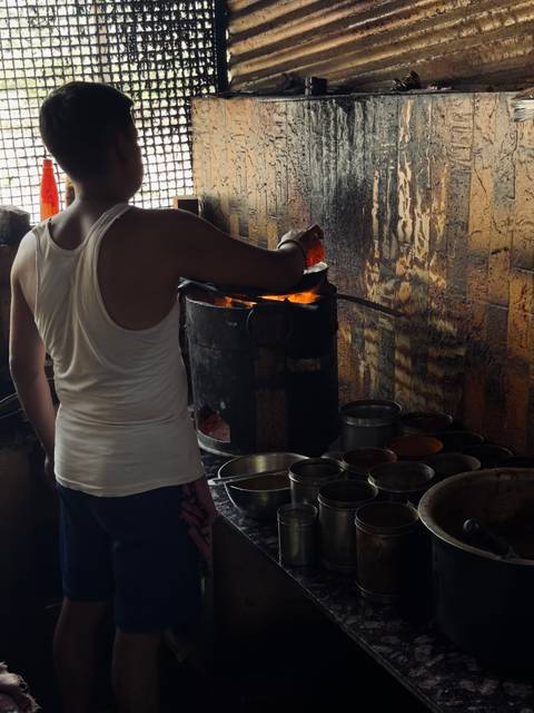 Street vendor stirs a glowing charcoal stove surrounded by metal spice tins