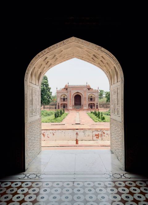 Symmetrical Mughal tomb framed by ornate marble archway with lush gardens ahead