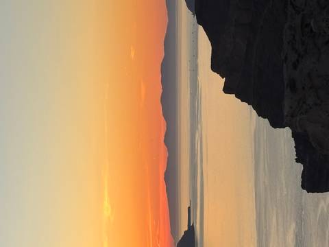 A vivid sunset over calm sea waters with dark silhouettes of distant islands beneath an orange and pink sky.