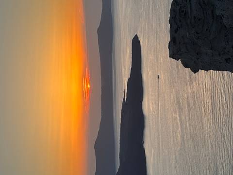 Golden sun setting behind island ridges, casting warm light over a shimmering sea with a lone boat below.