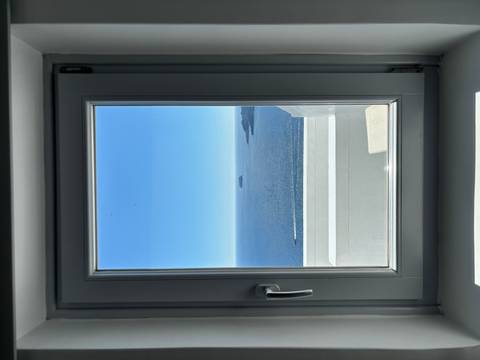 Sea view framed by a window overlooking a distant islet and the caldera’s blue waters.