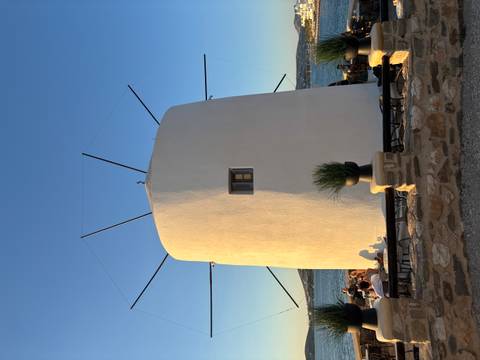 Traditional white windmill at sunset with patrons seated at an outdoor café around its base.