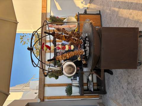 Outdoor chef grills long skewers of meat and vegetables on a round open flame in a market setting.