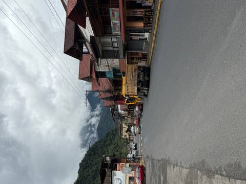 A mountain town main road under cloudy skies with timber-roofed buildings and vehicles parked along the asphalt.