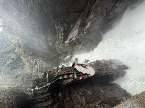 Visitors descend curved stone stairs beside the dramatic Pailon del Diablo gorge where a powerful river surges below misty cliffs.