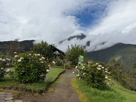 A flower-lined garden path leads toward cloud-shrouded volcano peaks rising above green valleys.