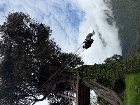 A traveler swings high from a treehouse platform overlooking misty mountains and clouds.