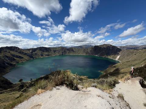 A panoramic view of Quilotoa’s turquoise crater lake surrounded by steep volcanic cliffs under a partly cloudy sky.