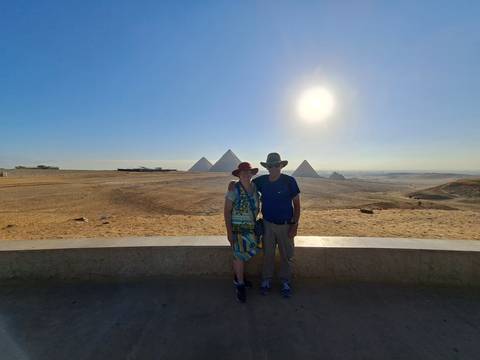 Smiling couple posing with the Pyramids of Giza under a bright sun.