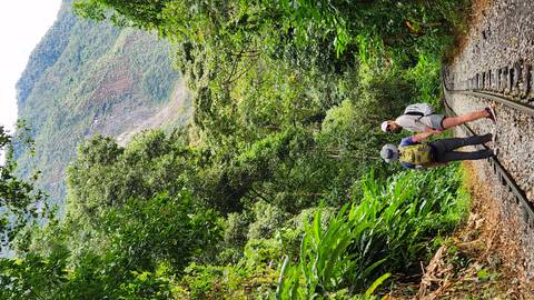 A couple walk hand in hand along jungle-lined railway tracks with green mountains towering ahead.