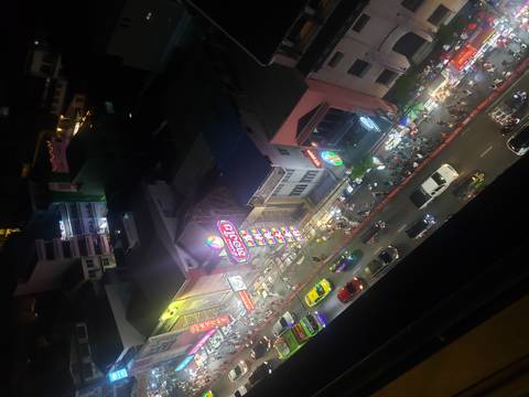 Night aerial of a busy neon-lit city street packed with cars, taxis, and pedestrians below tall buildings.