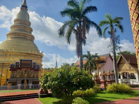 Golden temple stupa and palm trees rise above lush greenery beneath a bright tropical sky.