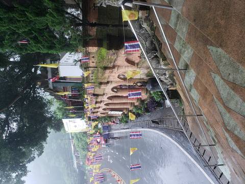 Rain-damp temple entrance lined with colorful flags and brick arches on a misty hillside road.