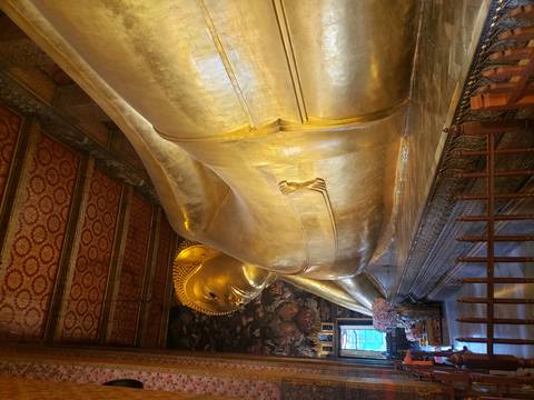 Interior view of an enormous gold reclining Buddha statue inside an ornately decorated hall.