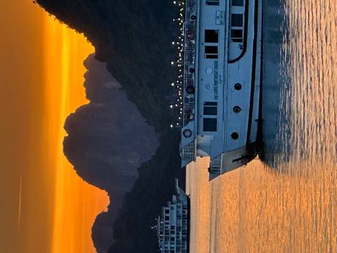 Cruise boats float on calm water beneath a fiery orange sunset with limestone karsts silhouetted behind.