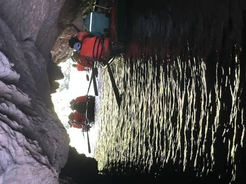 Rowboats of life-jacketed travelers paddle through a dim limestone cave toward daylight.
