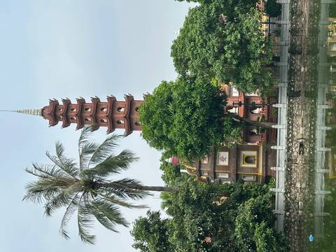 Tall red Tran Quoc pagoda rises behind palm trees and lush greenery beside a reflective pond.