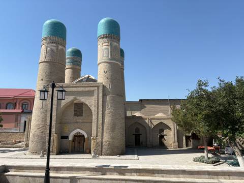 Historic Chor Minor mosque with four turquoise domes and brick facade under a bright blue sky.