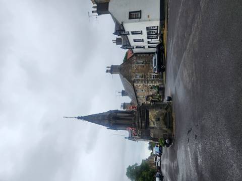 Quaint Scottish village square featuring historic stone buildings and a small monument.