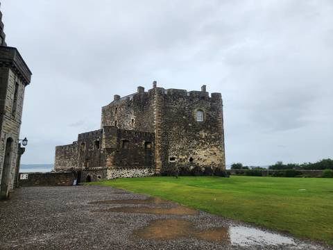 Robust stone castle beside green lawns and an estuary under gray skies.
