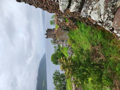 Ruins of Urquhart Castle overlooking Loch Ness surrounded by lush greenery.