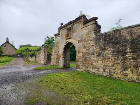Old stone arch gate leading to a country estate surrounded by greenery.