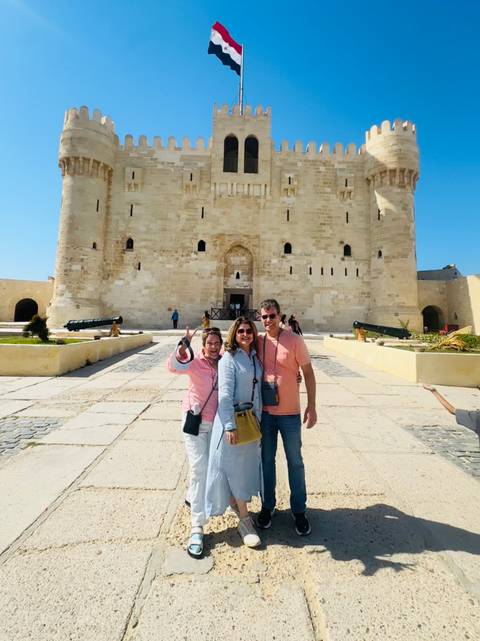 Three travellers pose happily before the massive stone walls and cannons of Alexandria’s Qaitbay Citadel.