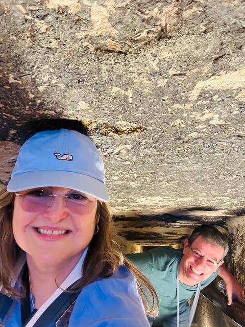 Close-cropped selfie of a woman under a low ancient stone ceiling, cap brushing the roof.