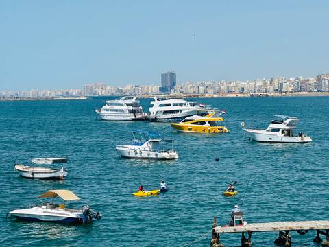 Various pleasure boats and kayakers dot the blue Mediterranean with Alexandria skyline in the background.
