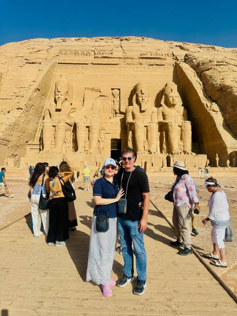 Travellers explore and pose before the colossal statues of Abu Simbel carved into sandstone cliffs.