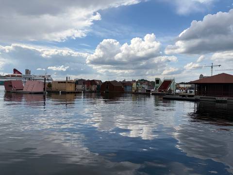 Calm waterfront scene with floating saunas, boats and dramatic clouds reflected on the water in Oslo harbour.