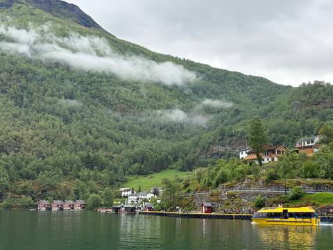 Fjord village with misty green hills, red boathouses and calm water dotted with excursion craft.