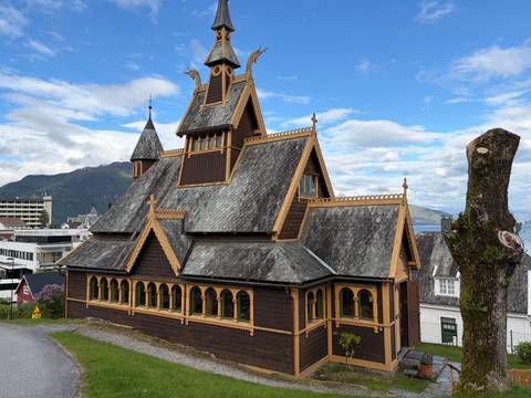 Historic wooden stave church with steep gables and carved dragon heads set against a blue sky.