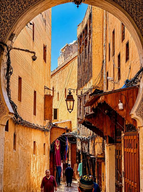 Narrow alleyway in a Moroccan medina with warm orange walls, hanging lanterns, and intricate wooden balconies.