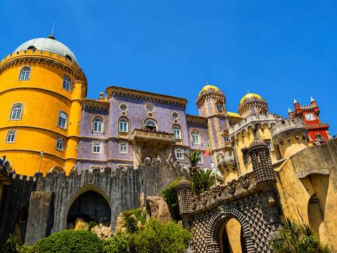 Bright yellow and purple towers of Pena Palace rise above ornate stone walls under a clear blue sky in Sintra.