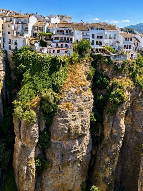 Steep rocky gorge covered in lush vegetation with a partial view of the historic stone bridge in Ronda.