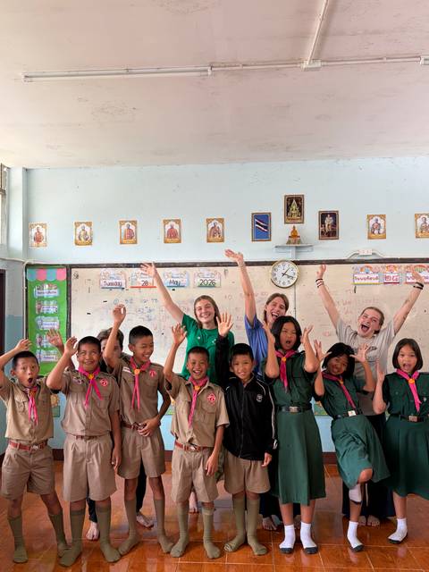 Volunteers and schoolchildren cheer in a colorful classroom decorated with Thai icons.