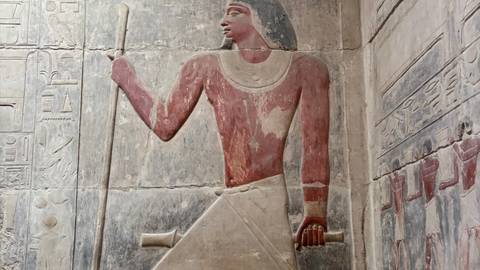 Ancient painted relief of an Egyptian noble holding a staff inside a tomb.