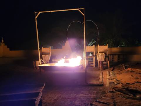 Nighttime desert campfire burning in metal tray surrounded by traditional stools and drums.