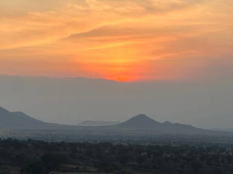 Serengeti plains silhouetted against a vivid orange sunset with soft mountain outlines.