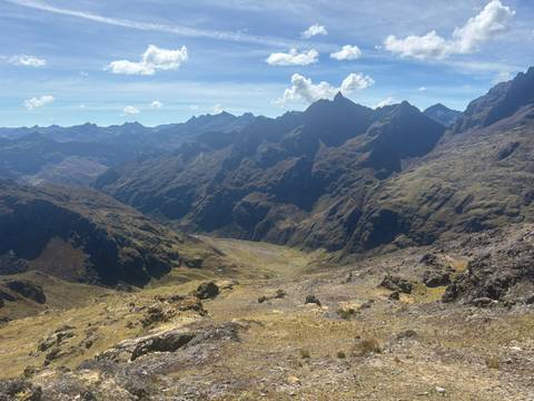 High-altitude Andean valley featuring rugged peaks, rolling ridges and a winding river under a bright sky.
