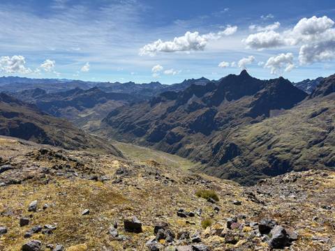 Expansive view of the Andes with jagged ridges, deep valleys and scattered clouds in a bright blue sky.