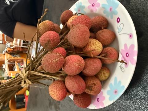 A bundle of fresh lychees rests on a floral plate atop a dark table indoors.