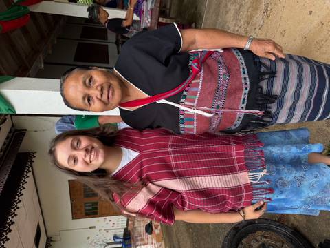 A young traveller and an elder local woman pose together wearing traditional woven garments.