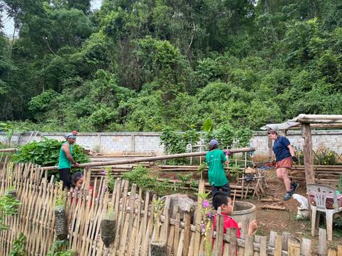 Volunteers work in a terraced garden bordered by bamboo fencing at the edge of dense jungle.