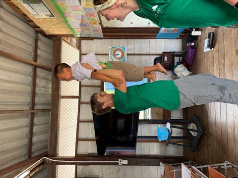 A volunteer lifts a laughing schoolboy inside a simple classroom.