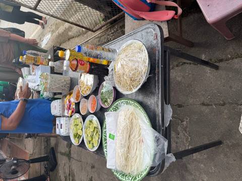 An outdoor table is set with noodles, lime wedges, sauces and ingredients for cooking.