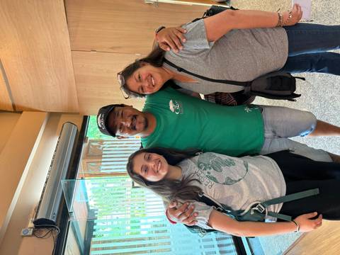 Two travellers hug their smiling local guide inside a modern lobby.