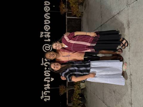 Three travellers pose at night in front of large Thai lettering on a terrace.