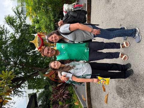 Travellers pose with their smiling guide outside a small shrine surrounded by tropical plants.